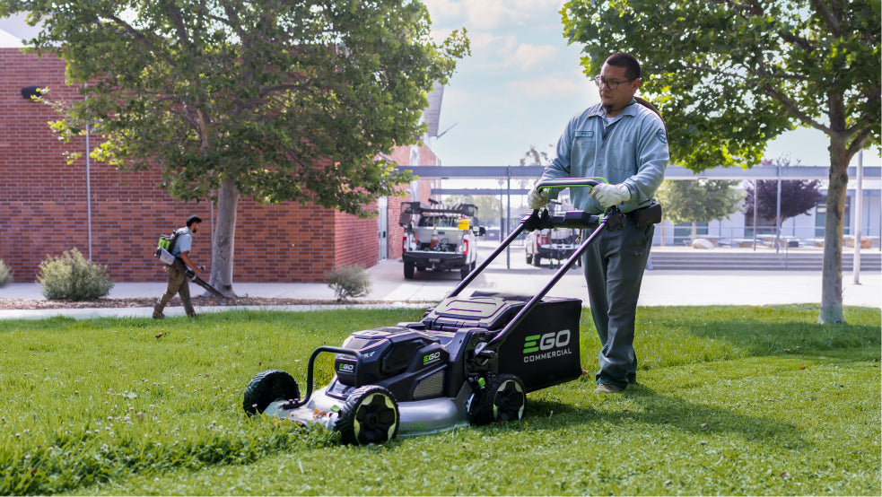 Person using an EGO lawn mower on a grassy area with a cityscape in the background